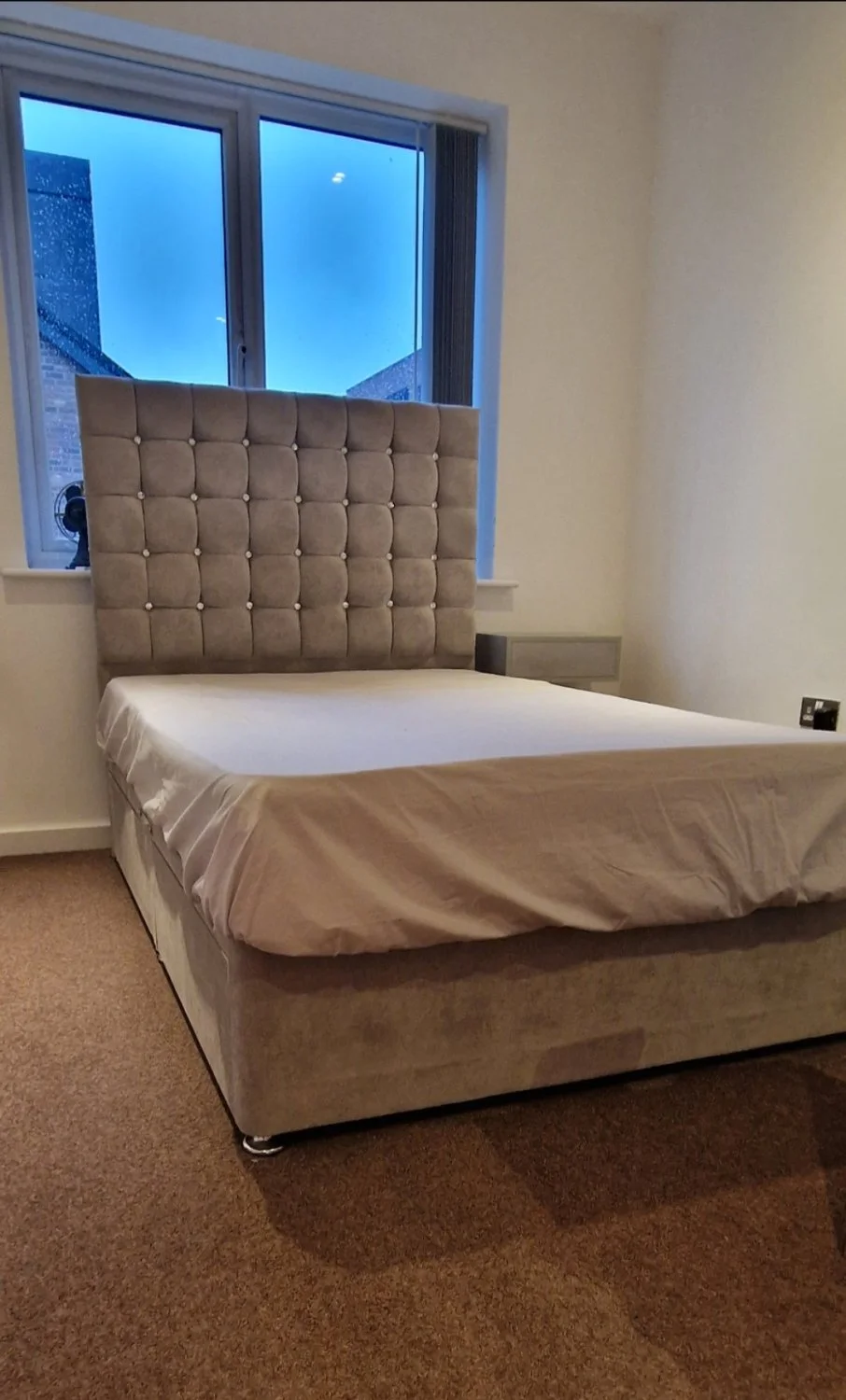 Grey upholstered storage divan bed with tall button-tufted headboard